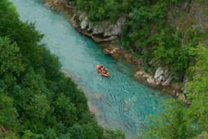 Aerial view of a group rafting down a vibrant turquoise river in Montenegro, surrounded by lush greenery.