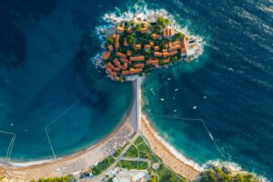 Stunning aerial photo of a coastal island with turquoise waters and vibrant roofed buildings.